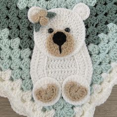 a crocheted teddy bear laying on top of a green and white afghan blanket