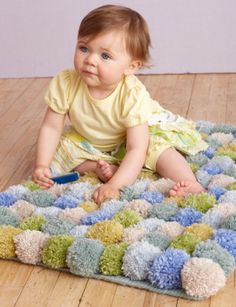 a baby sitting on the floor playing with a blue and green rug that looks like it has been made out of yarn