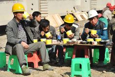 several people sitting around a table with cups and mugs in their hands while wearing hard hats