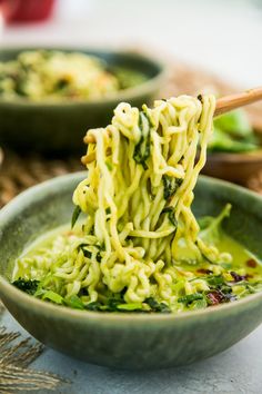 the noodles are being lifted by chopsticks from a bowl filled with broccoli