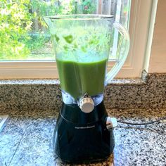 a blender filled with green liquid sitting on top of a counter next to a window