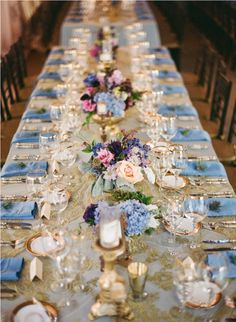 a long table is set with blue and white linens, silverware and flowers