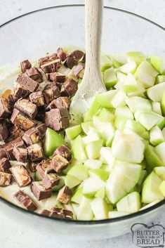 chopped apples and cubed meat in a glass bowl with a wooden spoon on the side