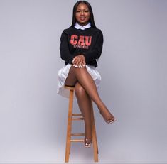 a woman sitting on top of a wooden stool wearing a black sweater and white skirt