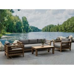 a couch, table and chair sitting next to a body of water with trees in the background