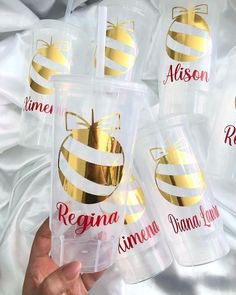 four plastic cups with gold foiled designs and name on the lids are being held by someone's hand