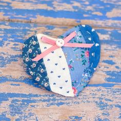 a blue heart shaped box with pink ribbon and bow on it sitting on a wooden surface