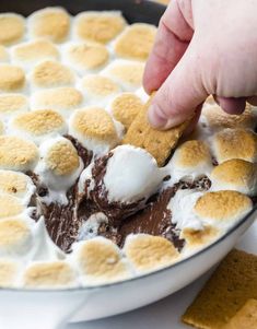 a person dipping marshmallows into a bowl of chocolate and graham crackers