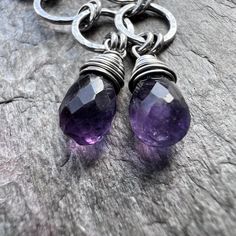 Two genuine amethyst teardrops have been wrapped in sterling silver wire. The natural stones hang from a set of sterling silver circles which I have formed, soldered, and hammered by hand. The earrings dangle from handmade sterling silver earwires. The silver has been oxidized and polished to create an antique patina finish. Be sure to see all photos and video for size and color reference. Amethyst Size: About 5x8mmTotal Earring Length (Including Earwire): Just under 2.25"Earring Weight: About 1 Purple Sterling Silver Teardrop Dangle Earrings, Purple Amethyst Drop Teardrop Earrings, Purple Amethyst Teardrop Earrings, Purple Sterling Silver Teardrop Earrings, Purple Sterling Silver Teardrop Earrings For Gift, Silver Amethyst Teardrop Jewelry, Silver Teardrop Amethyst Jewelry, Purple Gemstone Teardrop Dangle Earrings, Sterling Silver Teardrop Earrings With Natural Stones