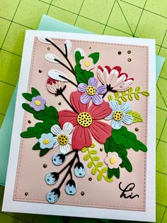 a close up of a card with flowers and leaves on the front, along with a green cutting board