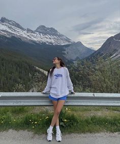 a woman is sitting on a bench in front of some mountains and snow capped peaks