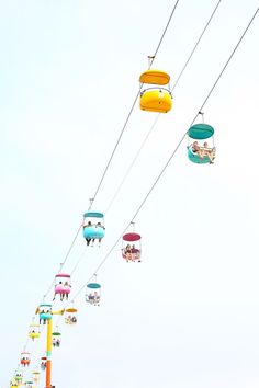 several colorfully decorated gondolas hang from wires in an amusement park, against a blue sky