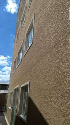 an apartment building with several windows and no doors on the outside, against a blue sky with white clouds