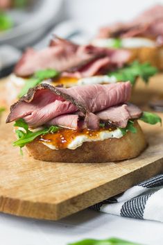 a wooden cutting board topped with sandwiches on top of a white table covered in green leafy garnish