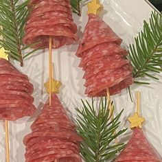 several slices of salami on sticks with pine needles and gold stars are arranged in the shape of christmas trees