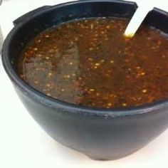 a black bowl filled with chili sauce on top of a white countertop next to a blender