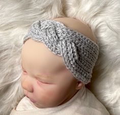 a baby wearing a knitted headband laying on top of a white fluffy blanket