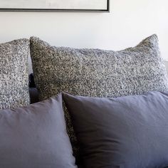 two gray pillows sitting on top of a bed next to a framed painting above them