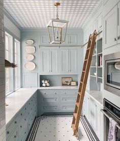 a ladder is in the middle of a kitchen with blue cabinets and white countertops