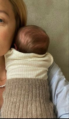 a woman holding a baby wrapped in a sweater and looking at the camera with her mouth open