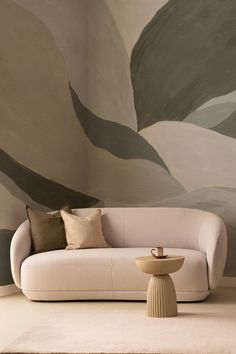 Modern living room with abstract earth-toned wallpaper, a soft beige sofa, and a minimalist side table with a coffee cup, creating a cozy and stylish decor. Leaf Mural, Quiet Luxury Aesthetic, Serene Living Room, Home Decor Ideas Modern, Muted Earth Tones, Soft Minimalism, Abstract Art Wallpaper, Moss Wall