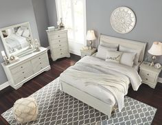 a white bed sitting on top of a wooden floor next to a dresser and mirror