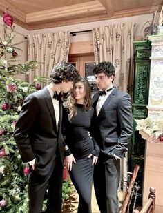 three people in formal wear standing next to a christmas tree