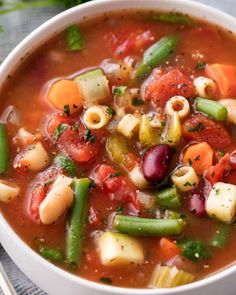 a white bowl filled with pasta and veggies soup on top of a table