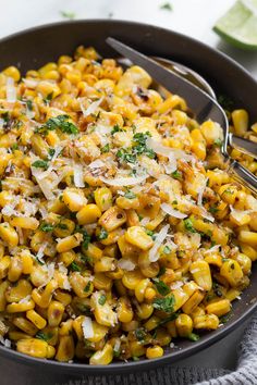 a skillet filled with pasta and cheese on top of a table next to lime wedges