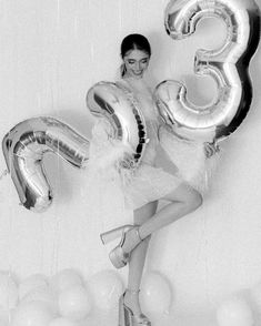 a woman is posing for a photo with balloons and the number three in front of her