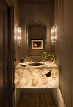 an elegant bathroom with marble counter tops and wood paneling, along with two lights on either side of the sink