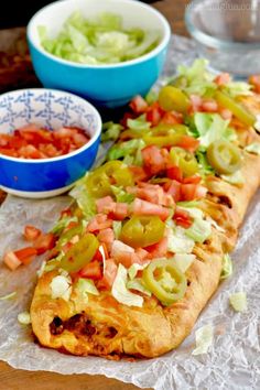 a long sandwich with tomatoes, lettuce and other toppings next to a bowl of salsa