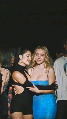 two women hugging each other in front of a group of people at a club or party