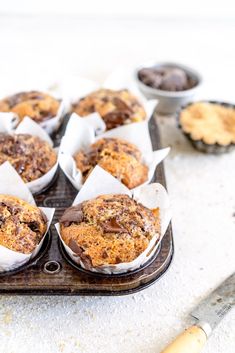 several muffins are sitting on a tray with paper wrappers around them and some chocolate chips in the background