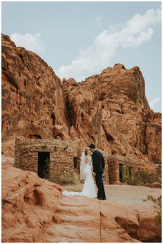 a bride and groom are standing in front of some rocky formations at the base of a mountain