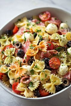 a white bowl filled with pasta salad on top of a marble countertop and topped with olives