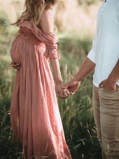 a pregnant woman holding the hand of a man in a long dress standing next to her