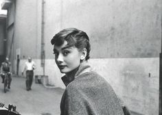 black and white photograph of a woman standing on the street with people walking behind her