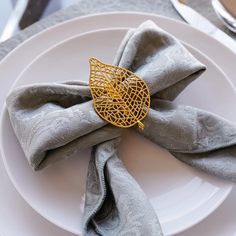 a white plate topped with a silver napkin and a gold brooch on top of it