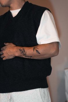 a man wearing a black vest and white shirt holding his arm with a tattoo on it