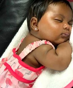 a small baby is sleeping on a white and pink blanket in a black leather chair