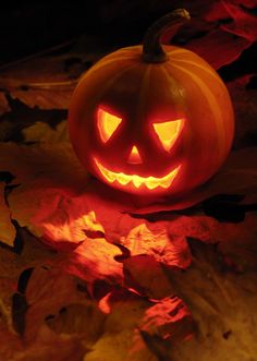 a lit up pumpkin sitting on top of leaves