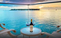 a bottle of wine sitting on top of a table next to two lounge chairs near the ocean