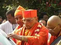 two men in orange robes standing next to each other and looking at something on the car