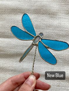 a hand holding a blue dragonfly pin