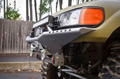 the front end of a vehicle parked in a driveway next to a fence and trees