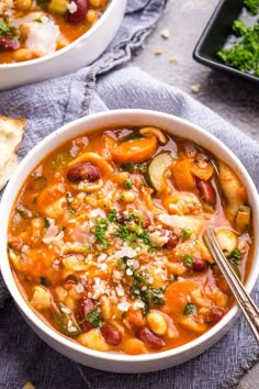 two bowls filled with beans and vegetables on top of a blue towel next to bread