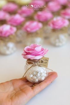 a hand holding a small glass vase with pink flowers in it and a tag on the top