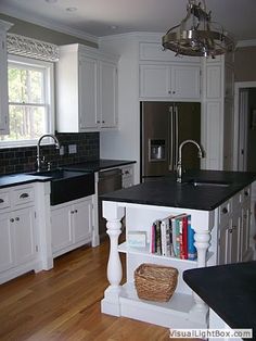 a kitchen with white cabinets and black counter tops, an island in the middle has books on it