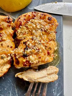 two pieces of meat sitting on top of a cutting board next to a knife and lemon